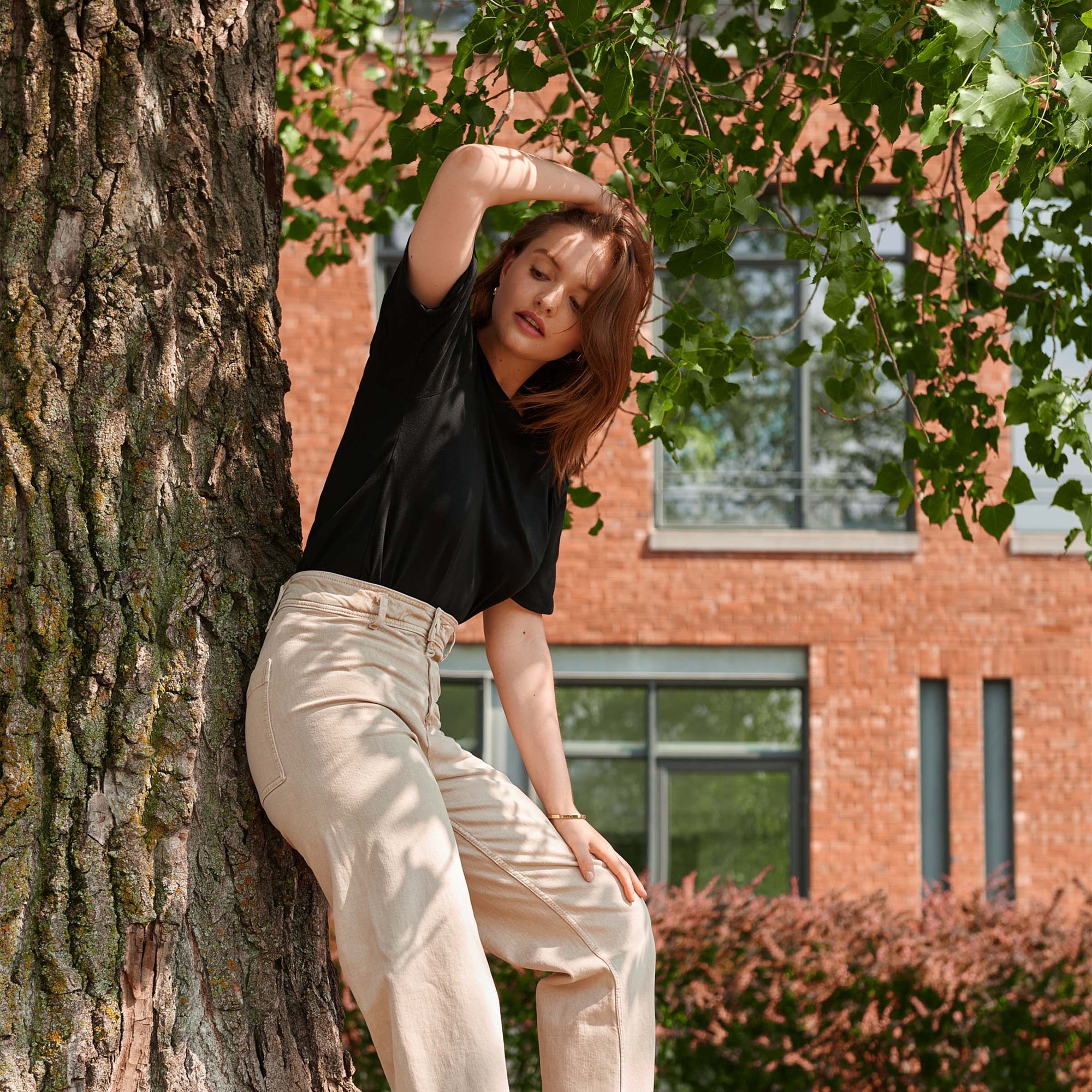 woman wearing sweatproof t-shirt in black leaning against tree