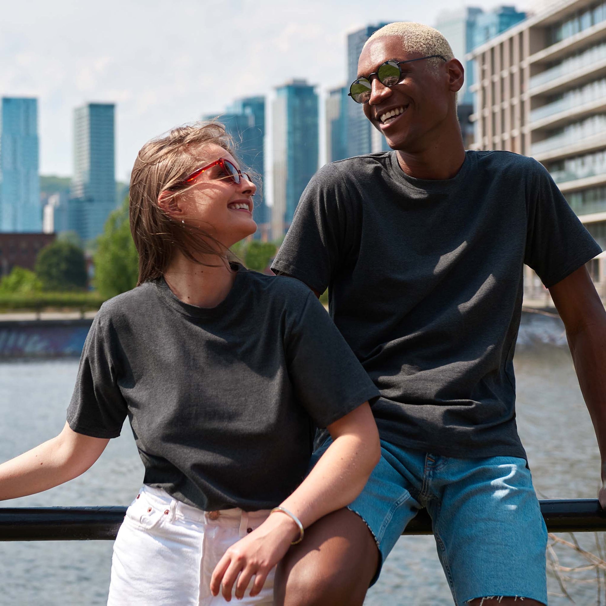 A man and woman in grey t-shirts looking at each other with a city background